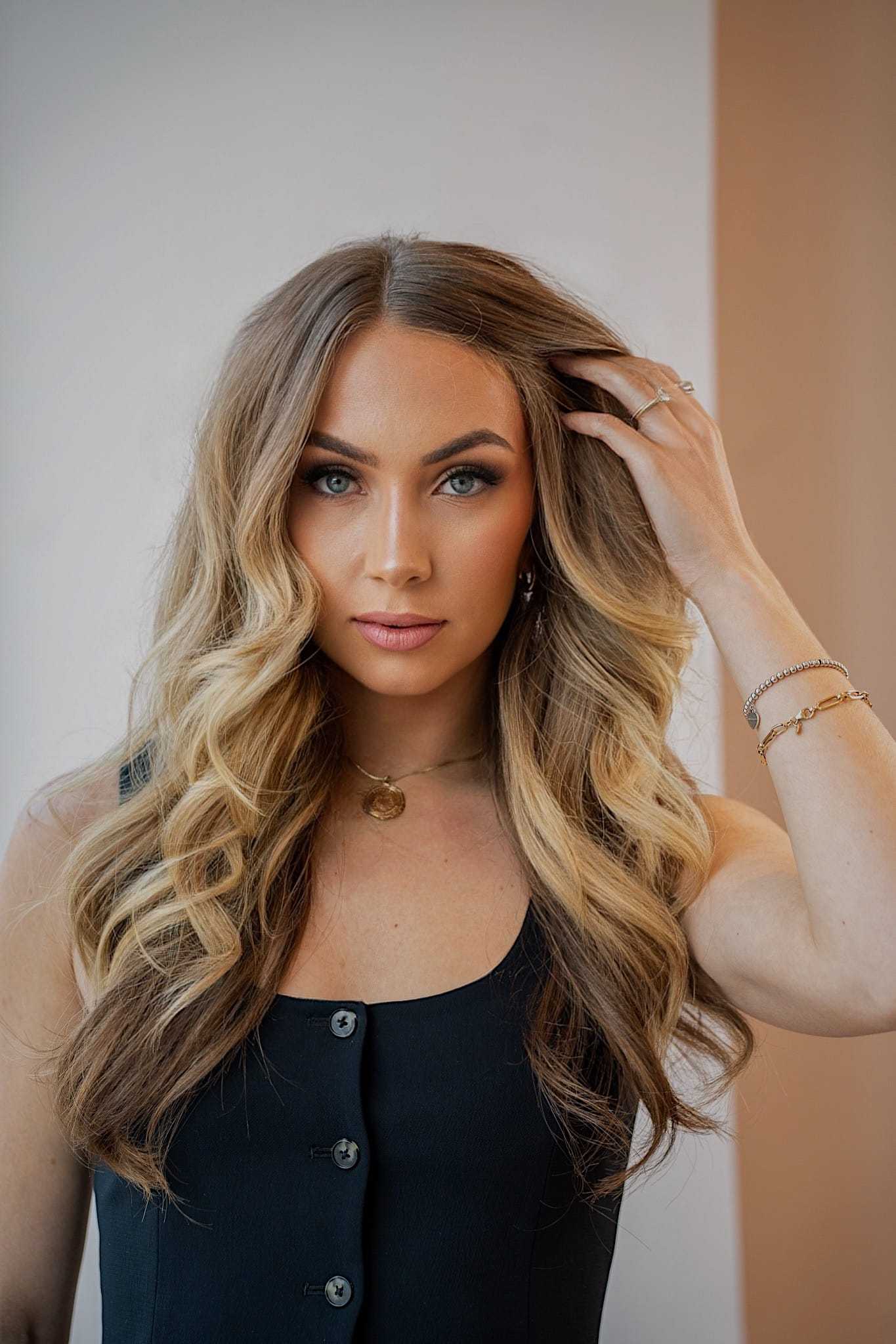 Woman with long, wavy hair in black dress poses with hand in hair.