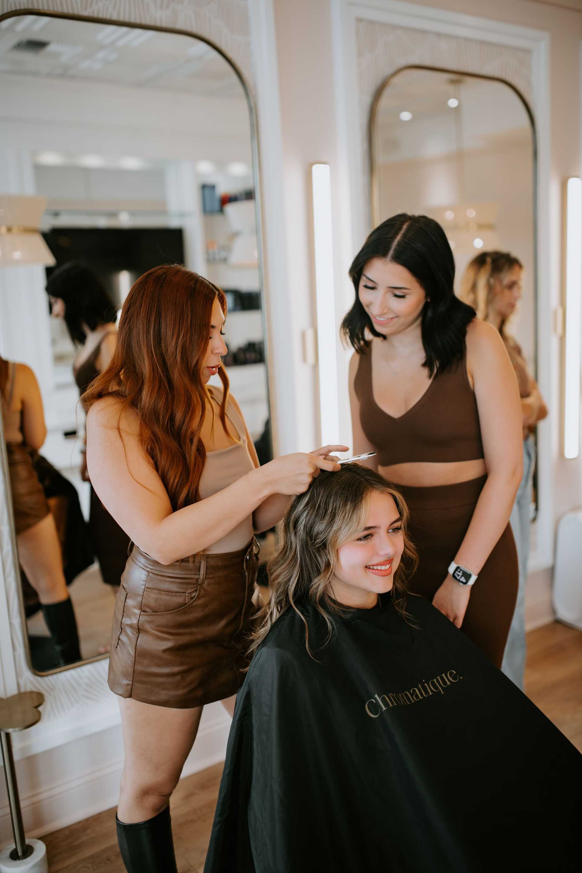 Two women styling another woman's hair in a modern salon setting.