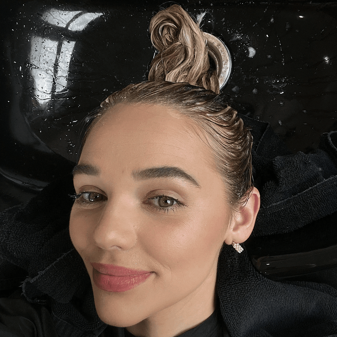 Woman with hair dye, smiling in a salon sink with black towels.