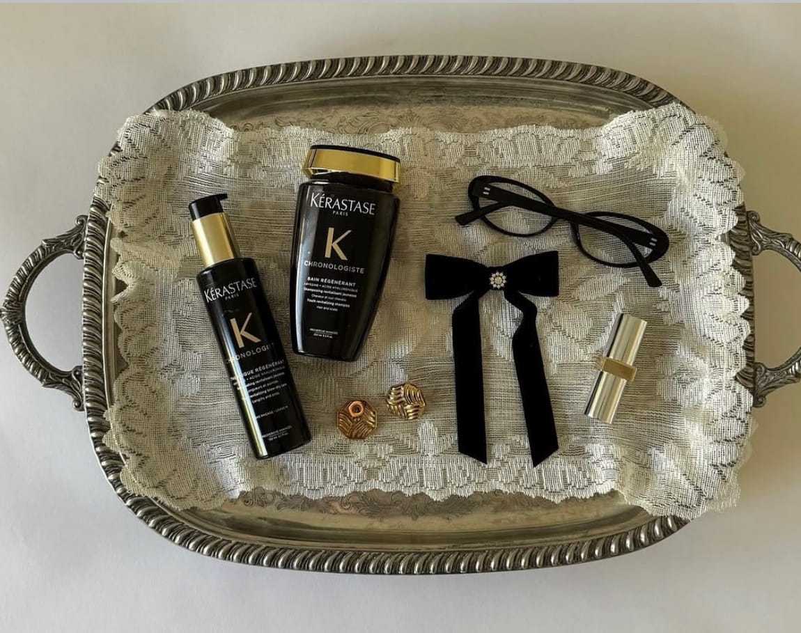 Tray with Kerastase products, glasses, a bow, earrings, and a lipstick on lace.