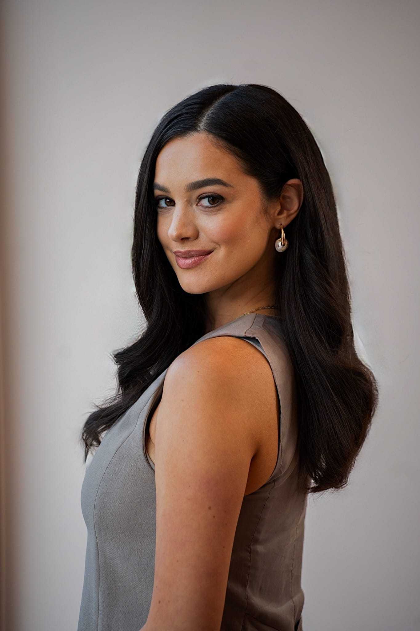 Woman smiling, wearing a sleeveless top, with long dark hair styled elegantly.