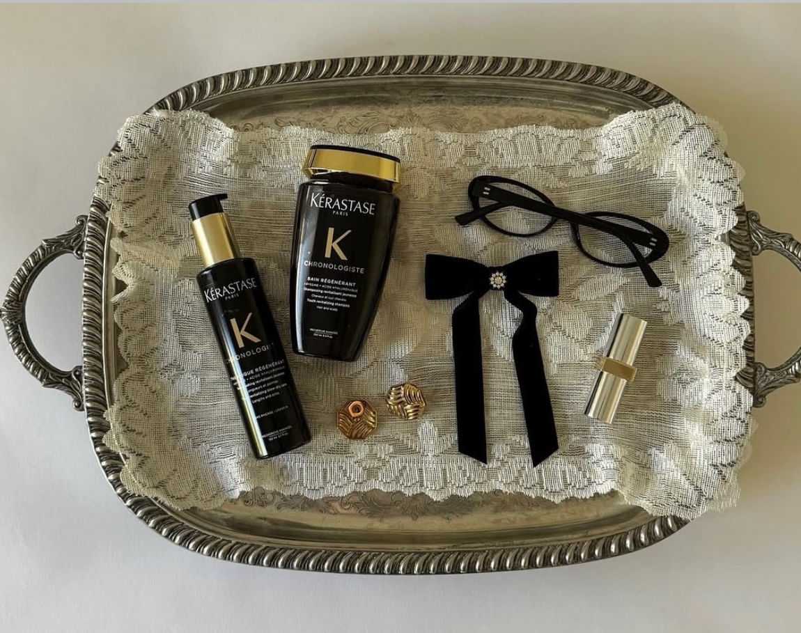 Tray with Kerastase products, glasses, a bow, earrings, and a lipstick on lace.