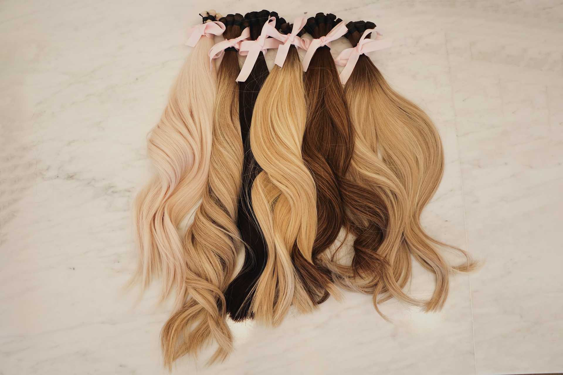 Luxurious hair extensions in various shades with pink bows on marble background.
