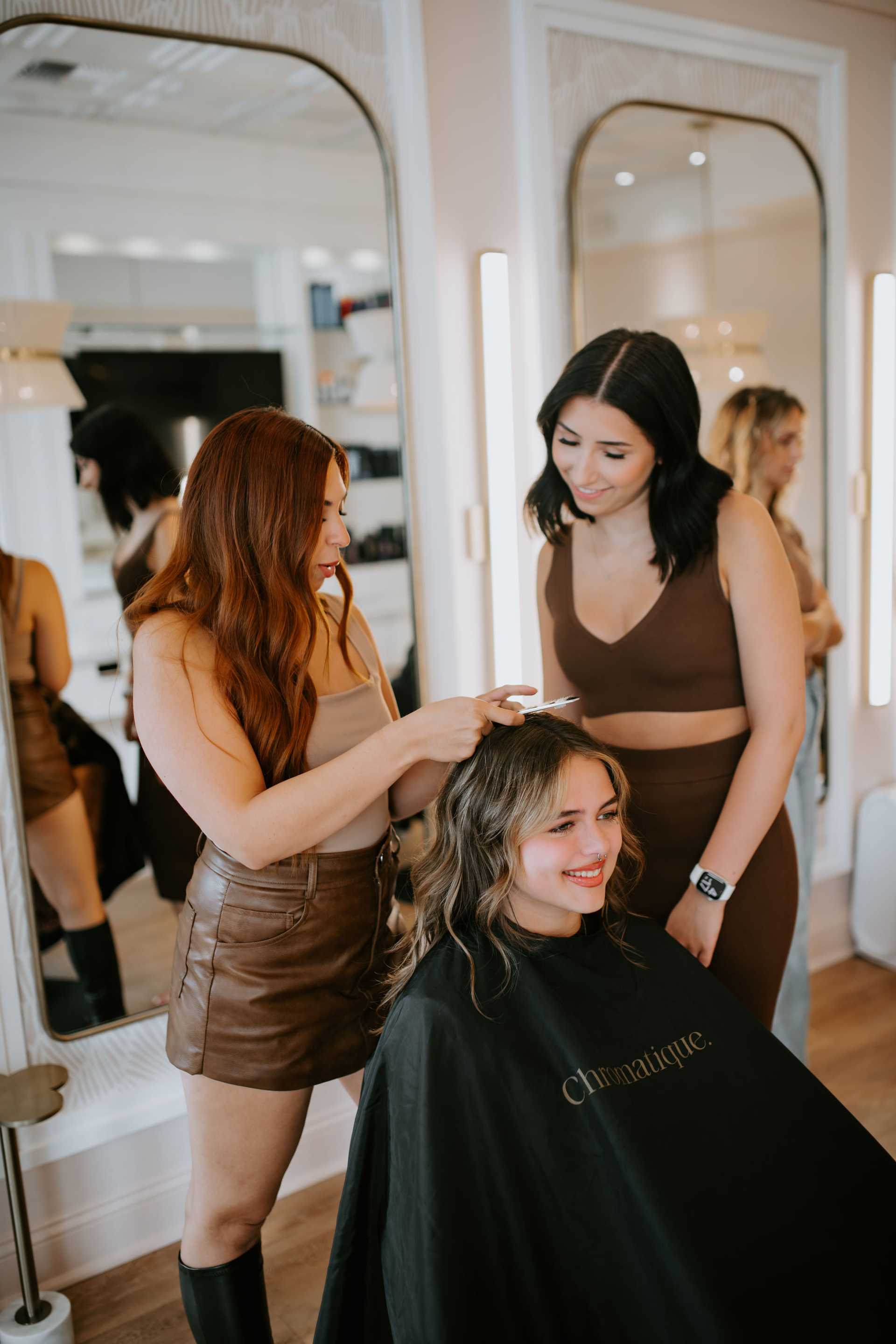 Two women styling another woman's hair in a modern salon setting.