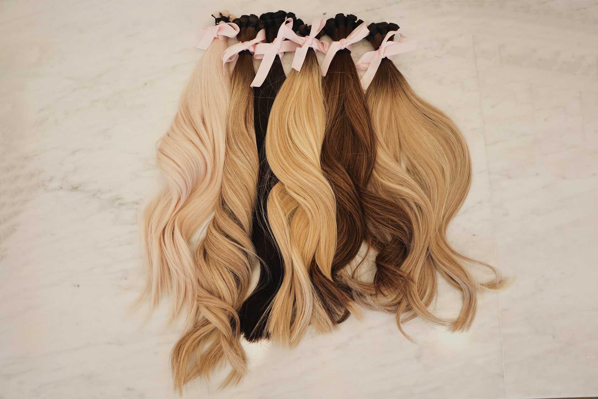 Luxurious hair extensions in various shades with pink bows on marble background.