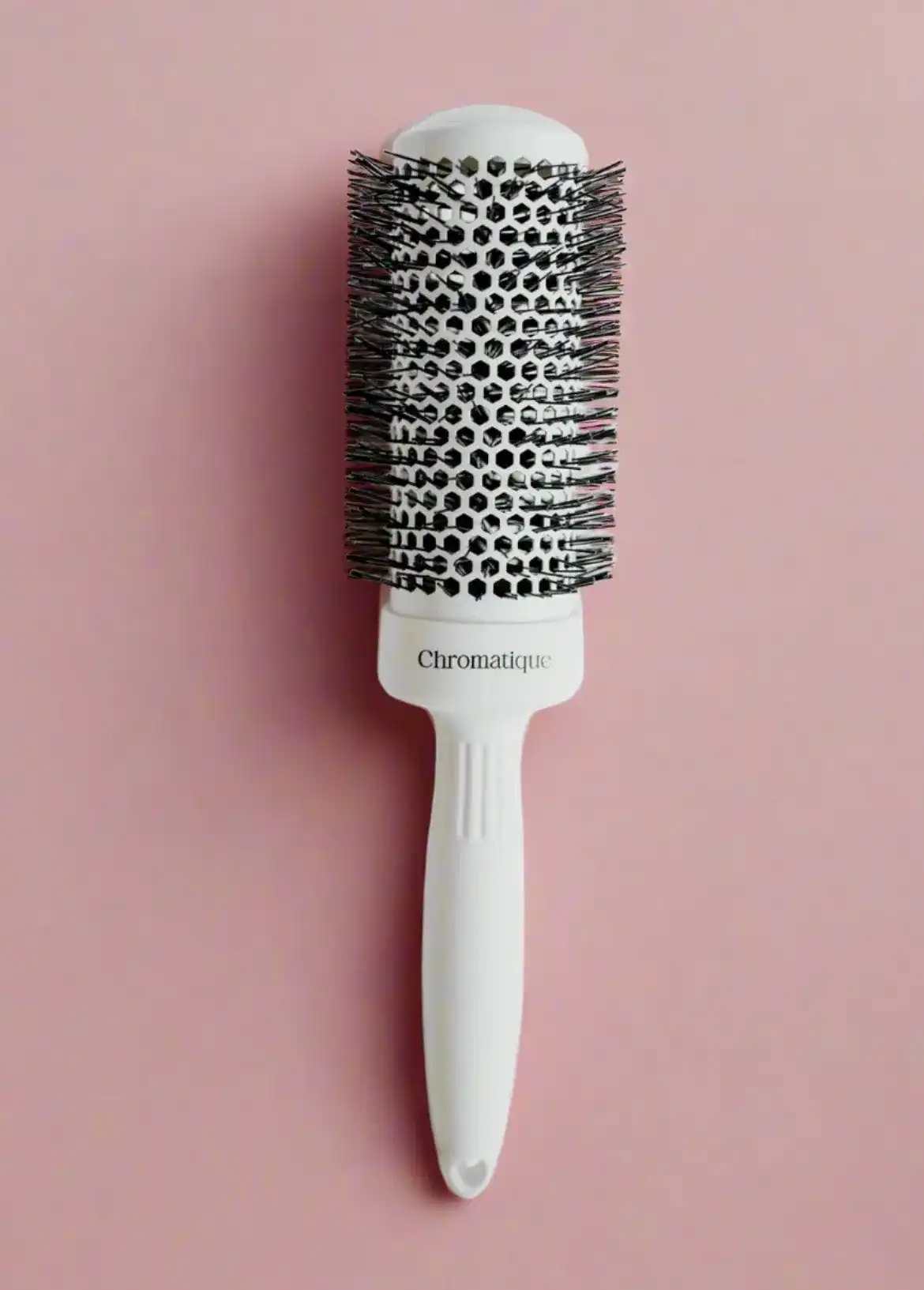 A round hairbrush with a white handle on a pink background.