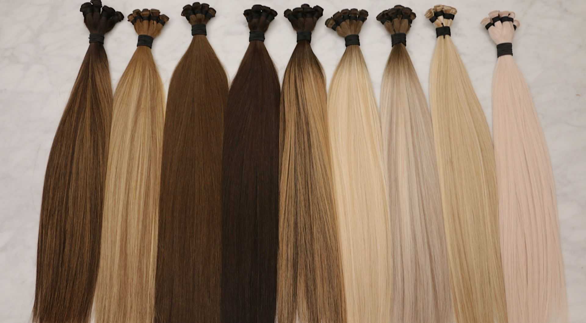 Hair extensions in various shades from dark brown to light blonde, displayed on a marble surface.