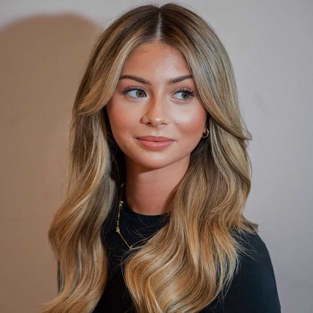Young woman with long, wavy blonde hair, wearing a black top, gazing to the side.